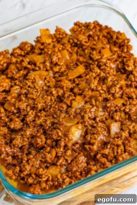 The savory meat mixture spread evenly over the golden-brown cornbread crust in a baking dish, forming the next layer of the Tamale Pie.