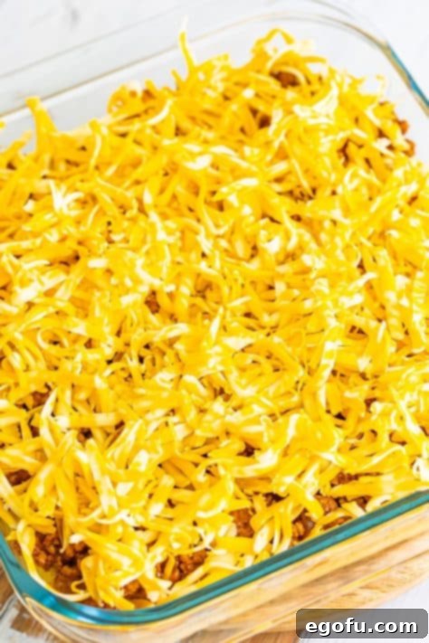 Shredded Colby Jack cheese generously layered on top of the meat mixture and cornbread crust in a baking dish, ready for its final bake.