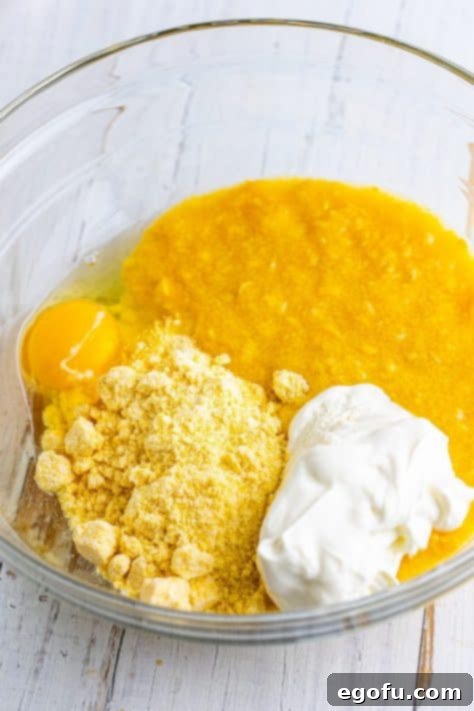 A bowl with cornbread mix, sour cream, egg, and creamed corn, being stirred to combine into a smooth batter.