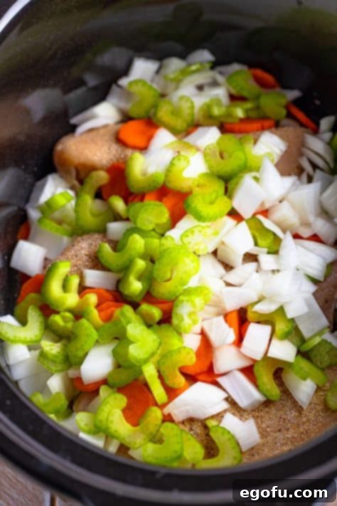 Carrots, celery, and onions on top of chicken in a CrockPot.