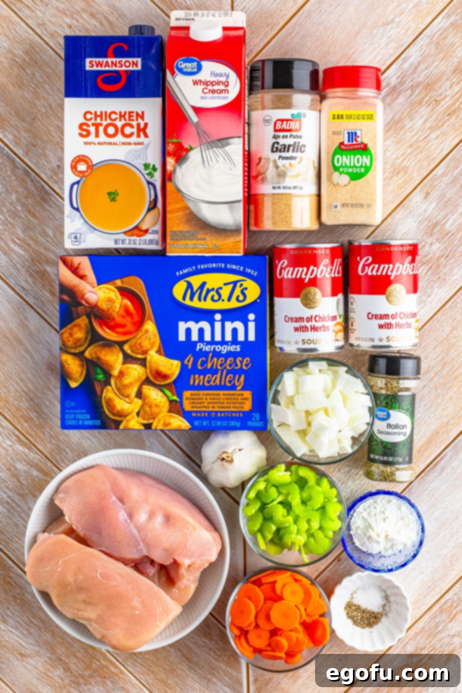 An array of ingredients laid out for Chicken Pierogi Stew: mini pierogies, chicken breasts, chicken stock, cream of chicken soup, sliced celery, black pepper, garlic powder, onion powder, salt, sliced carrots, diced onion, heavy cream, minced garlic, Italian seasoning, cornstarch, and water.