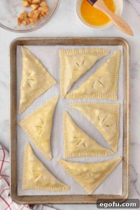 Filled unbaked apple turnovers on a baking sheet, with vent slits.
