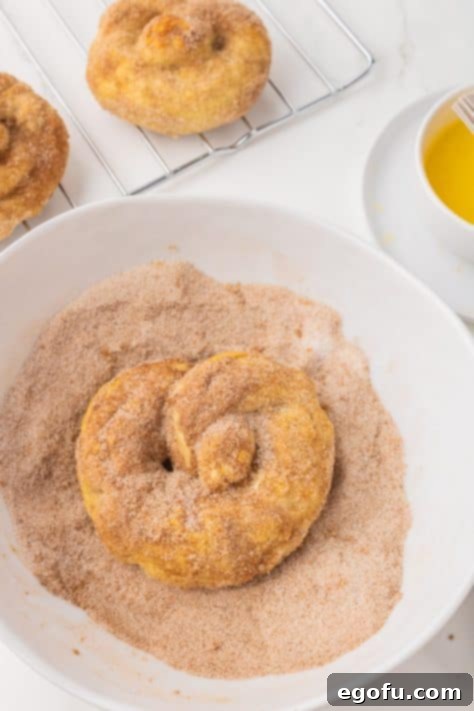 A baked pretzel being dipped into a bowl of cinnamon sugar mixture, ensuring a complete coating.