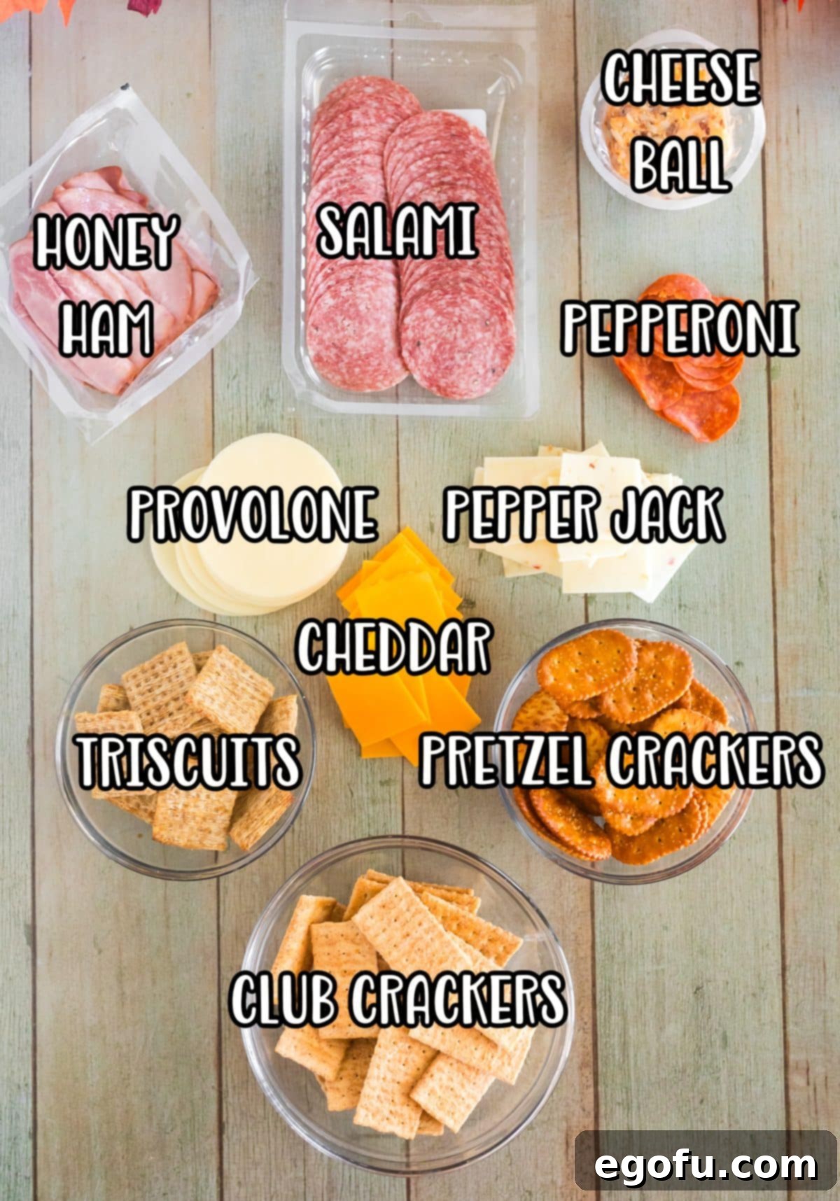 A vibrant array of Thanksgiving charcuterie board ingredients including Triscuits, various deli meats, Pepper Jack, cheddar, and provolone cheeses, pretzel crackers, club crackers, salami, pepperonis, and a cheeseball.