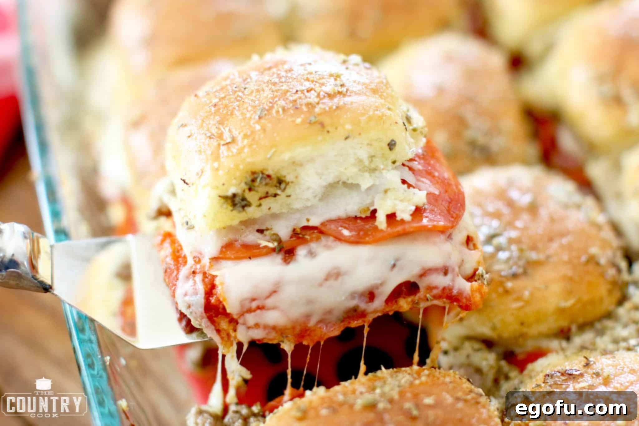 One pizza slider removed from a tray of cooked pizza pull apart sliders, showcasing its cheesy, savory layers.