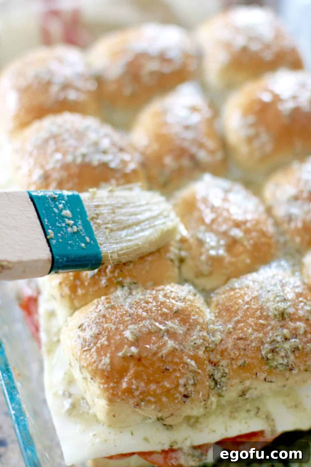 Brushing the flavorful garlic butter mixture over the top of the slider rolls.