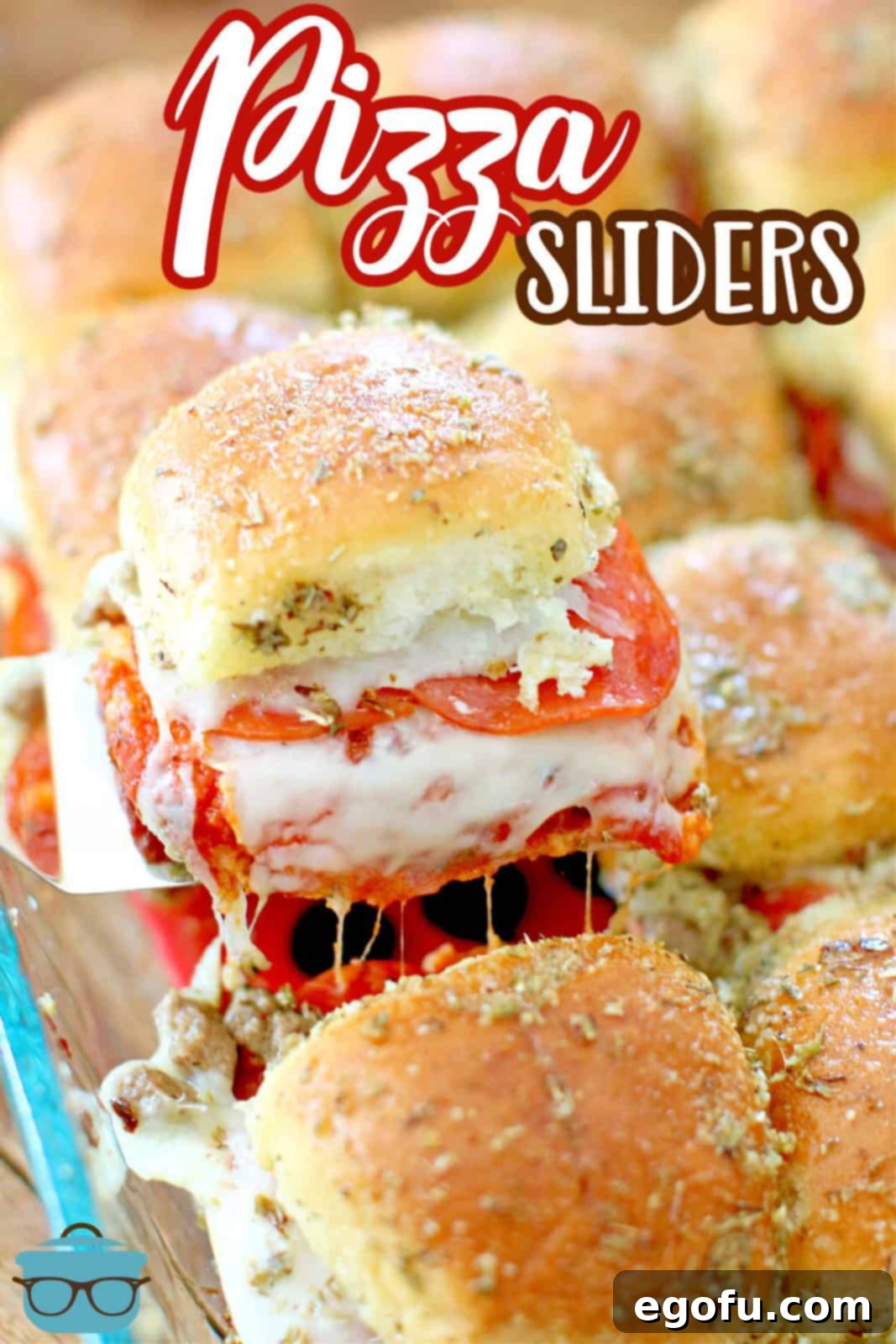 A spatula gently pulls a golden-brown pizza slider from the baking dish, revealing melted cheese and rich toppings.