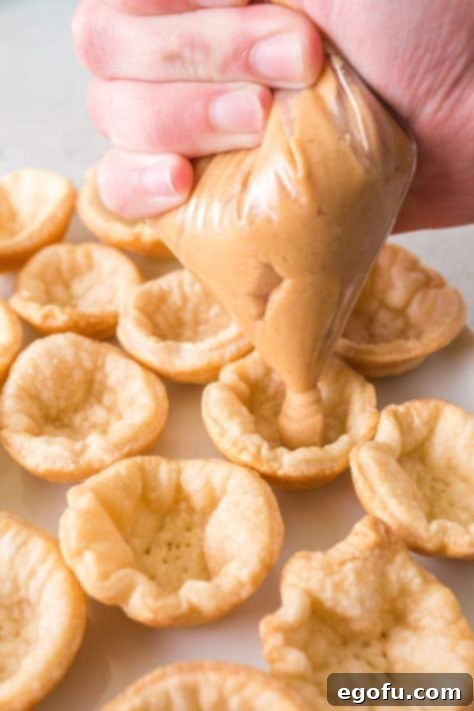 Mini pie crusts with a peanut butter mixture being pipped into them.