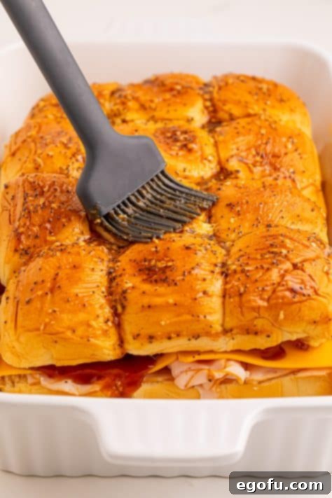 Zesty BBQ Chicken Sliders 16 A pastry brush brushing seasoning mixture on top of Hawaiian rolls.