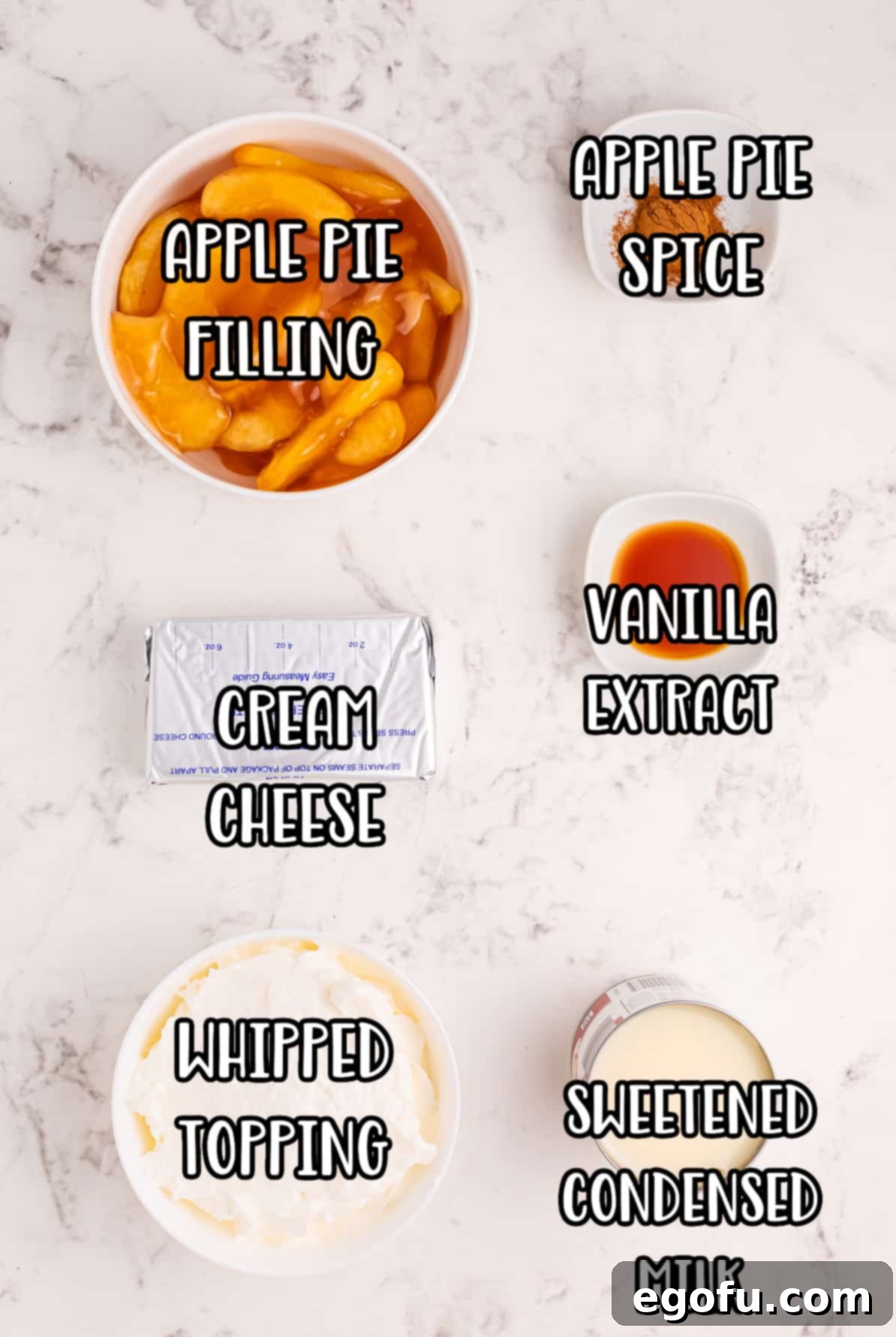 A beautiful flat lay of all the essential ingredients for Apple Pie Dip: apple pie filling, vanilla extract, apple pie spice, cream cheese, Cool Whip, and sweetened condensed milk.