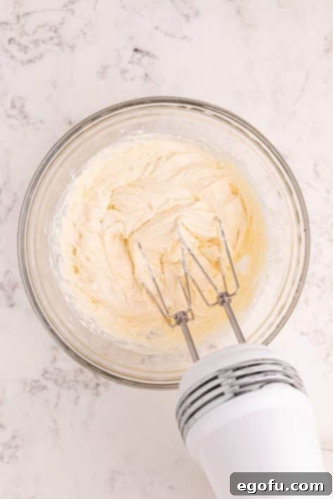 An electric mixer in a bowl of softened cream cheese, sweetened condensed milk and vanilla extract.