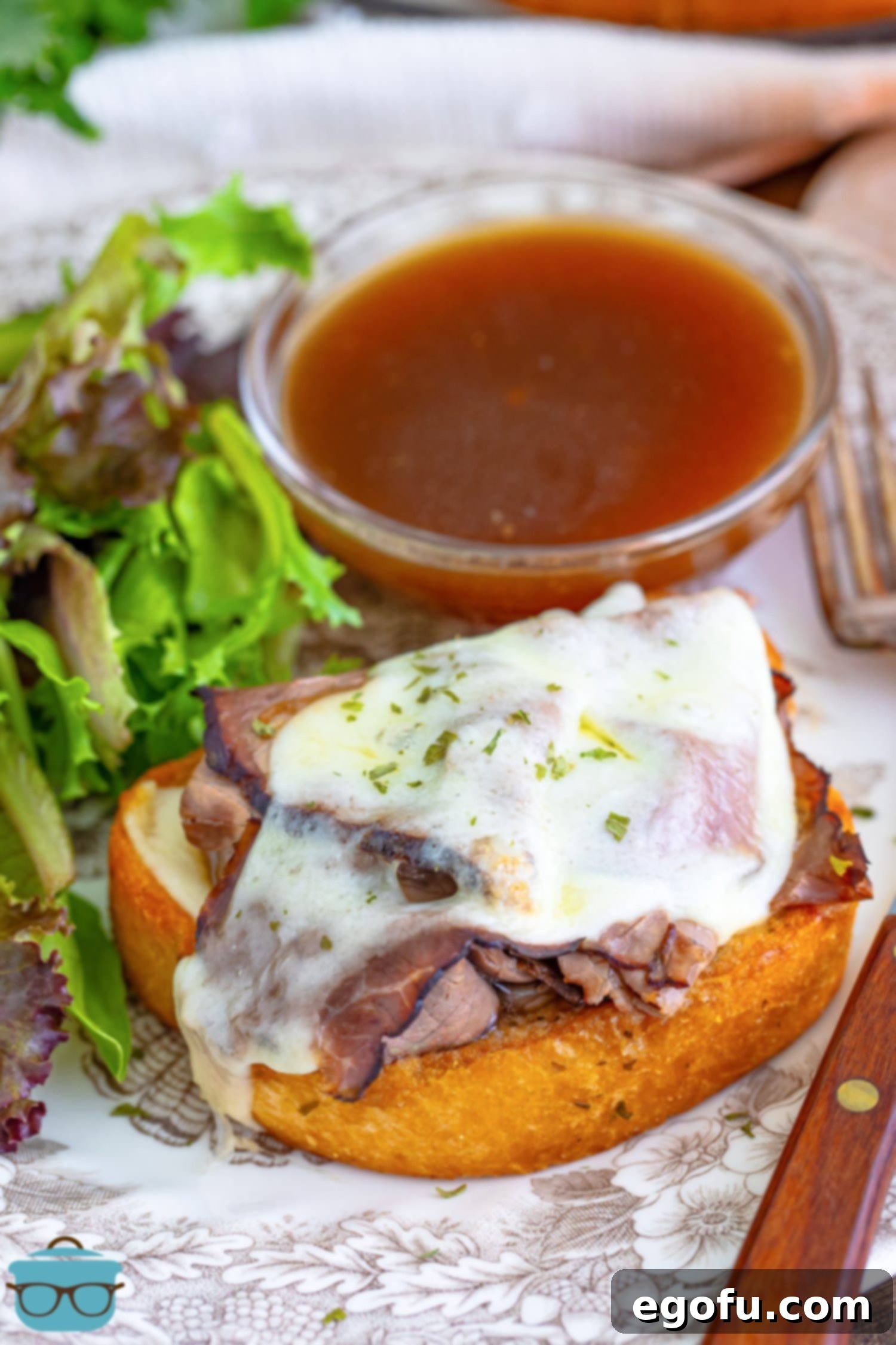 A perfectly prepared Texas Toast French Dip sandwich, generously filled with roast beef and melted provolone cheese, ready to be dipped in a small bowl of rich au jus gravy. The toast is golden brown and crispy.