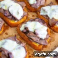 Closely looking down on a lined baking sheet with some Texas Toast French Dips, showing melted cheese and golden toast.