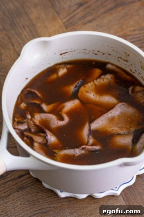 Thinly sliced roast beef warming in a pot of au jus gravy.