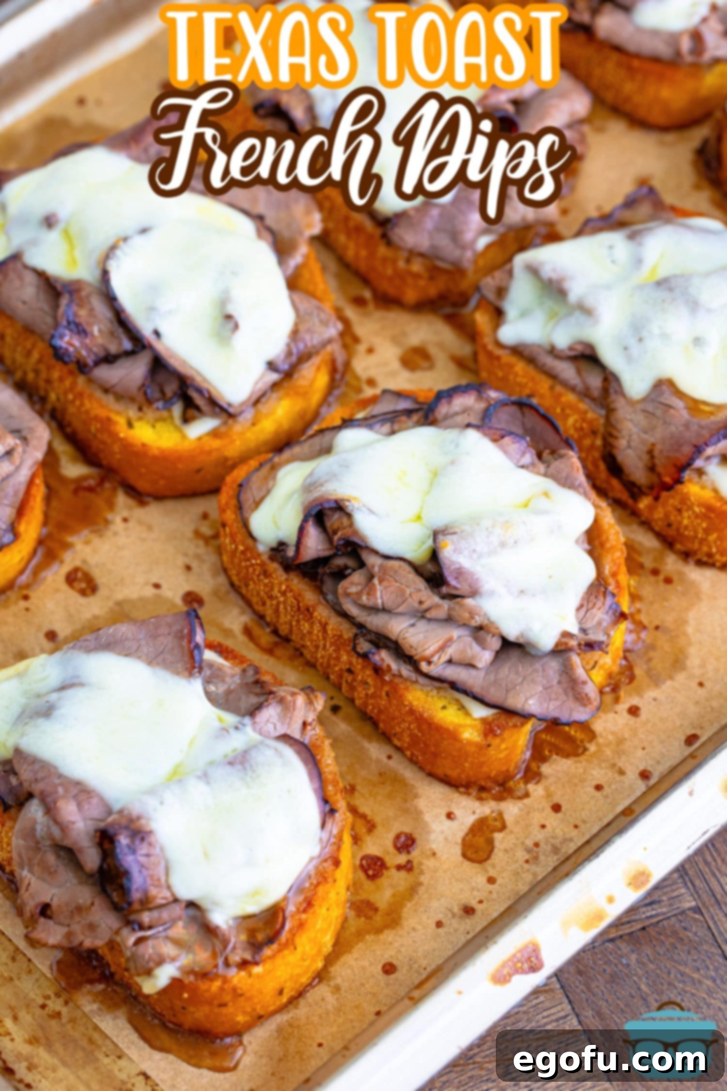 Freshly baked Texas Toast French Dips arranged neatly on a parchment-lined baking sheet, their melted cheese and roast beef gleaming, ready to be served.