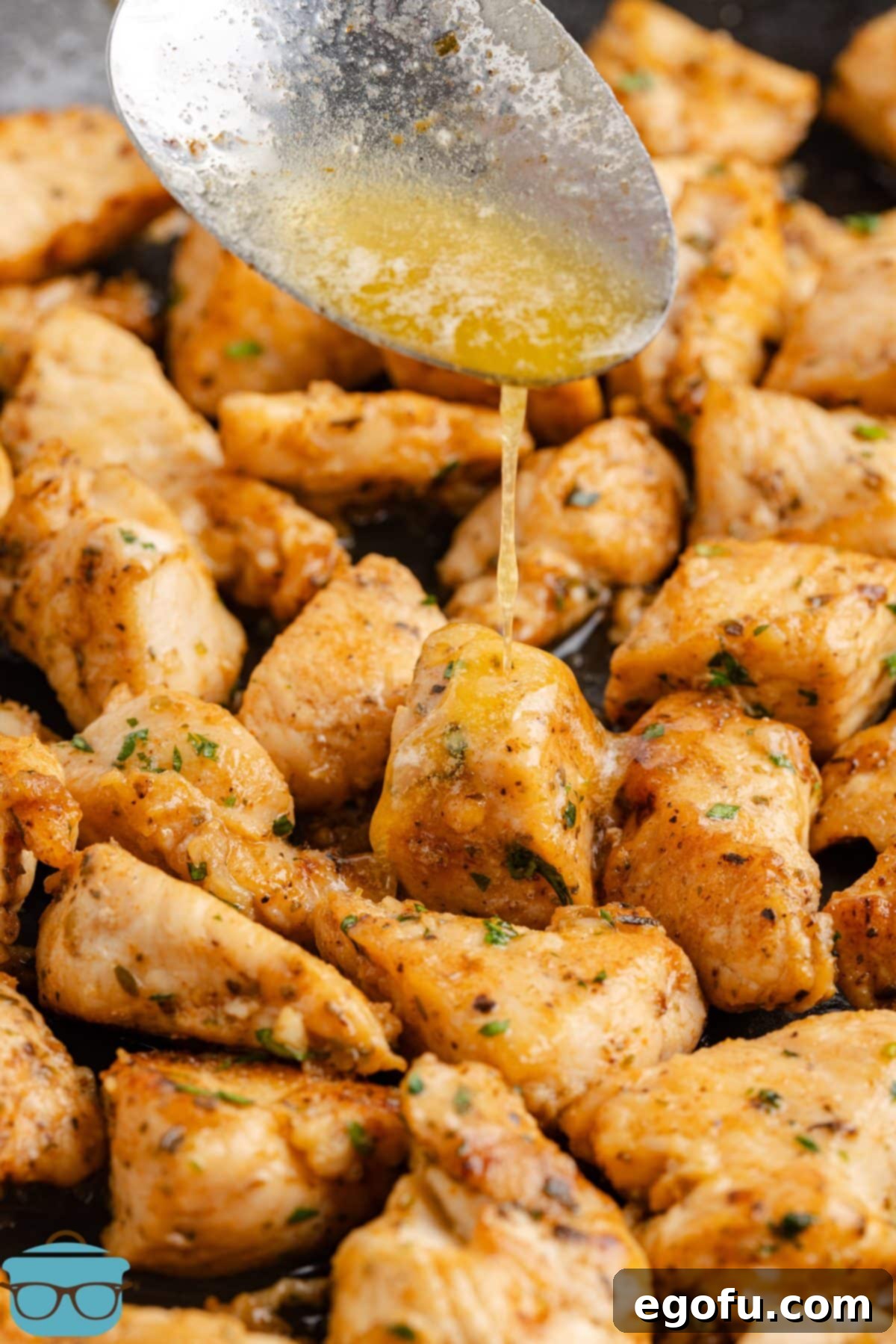 A spoon drizzling some garlic butter over the chicken bites in a skillet.