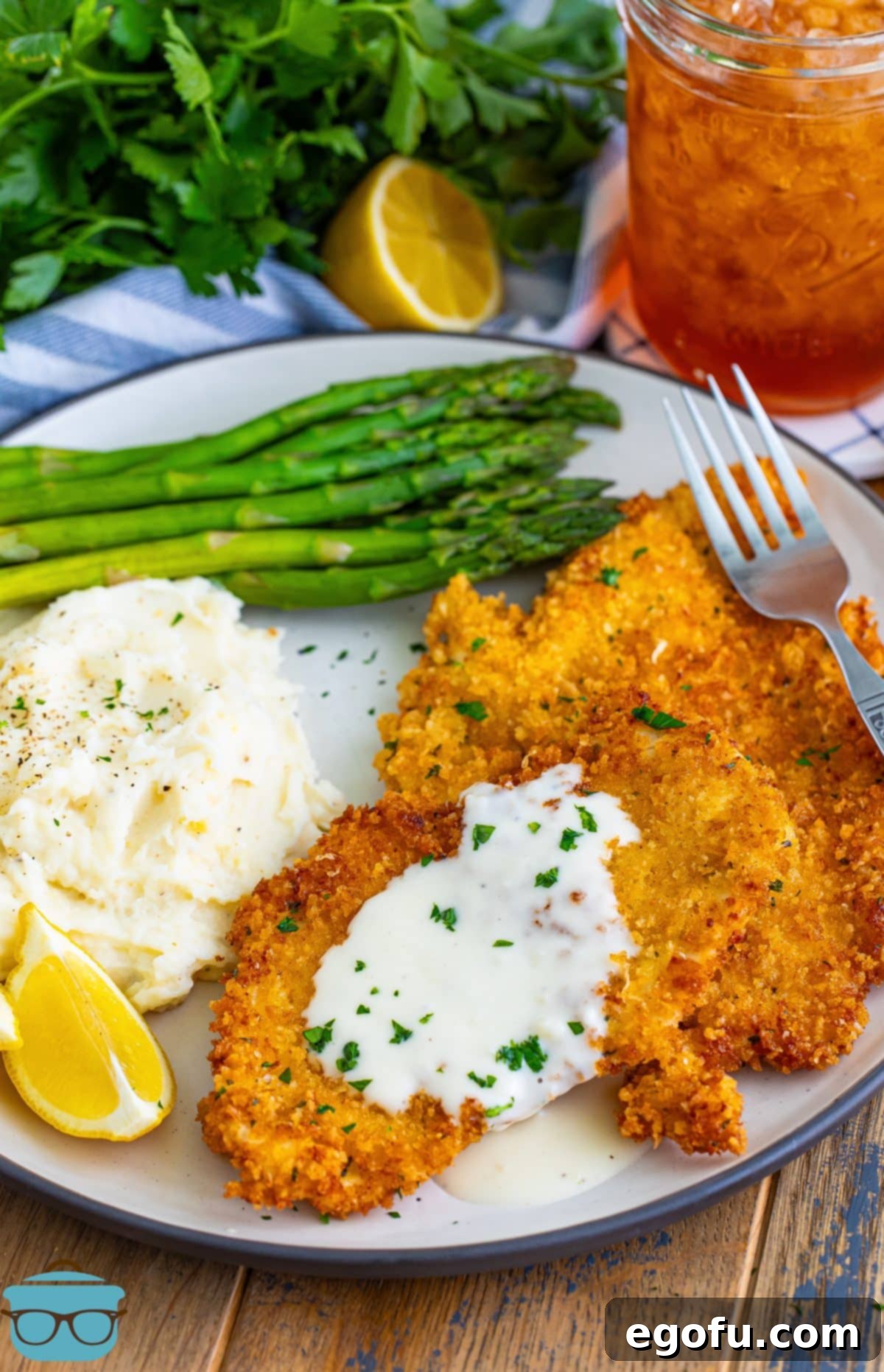 A plate with golden brown Chicken Costoletta, garnished with fresh parsley and served alongside crisp green asparagus spears, evoking a restaurant-quality presentation.