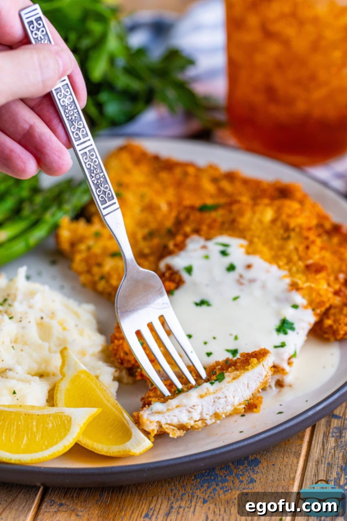 A fork gracefully piercing a slice of golden-brown Chicken Costoletta, inviting you to savor the first delectable bite of this homemade restaurant favorite.