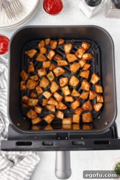 Crispy Air Fryer Breakfast Potatoes 11 Home Fries in an Air Fryer basket, halfway through cooking and turning golden.