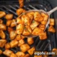 Crispy Air Fryer Breakfast Potatoes 8 A scoop of Air Fryer Home Fries above the air fryer basket, showing their appealing texture.