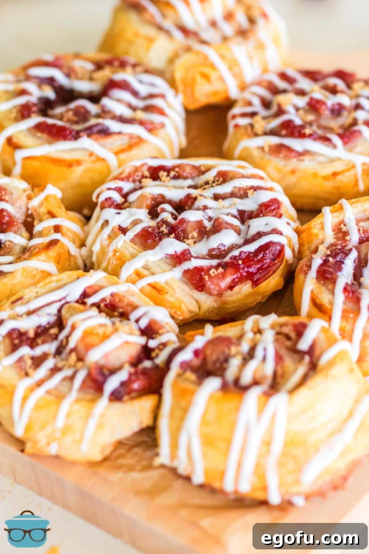 A small pile of golden-brown, flaky Cranberry Pinwheels, drizzled with vanilla icing.