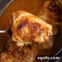 A serving utensil holding a Crock Pot Chicken Thigh above the rest of the Slow Cooker, highlighting its tenderness and the rich gravy.