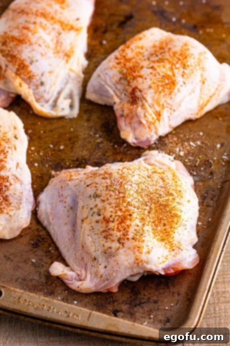 Seasoned chicken thighs on a baking sheet, ready for the pan.