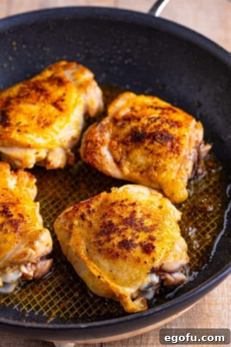 Chicken thighs searing in a pan.