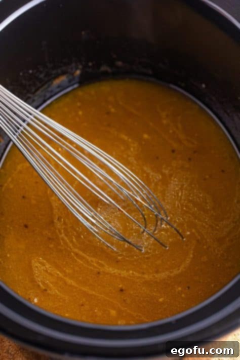 A whisk whisking in a cornstarch slurry into chicken gravy in a Crockpot.