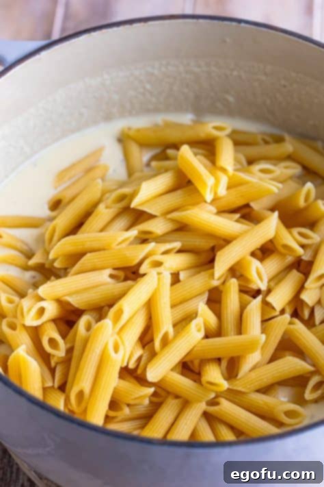 Cooked penne being added to a pot with sauce.
