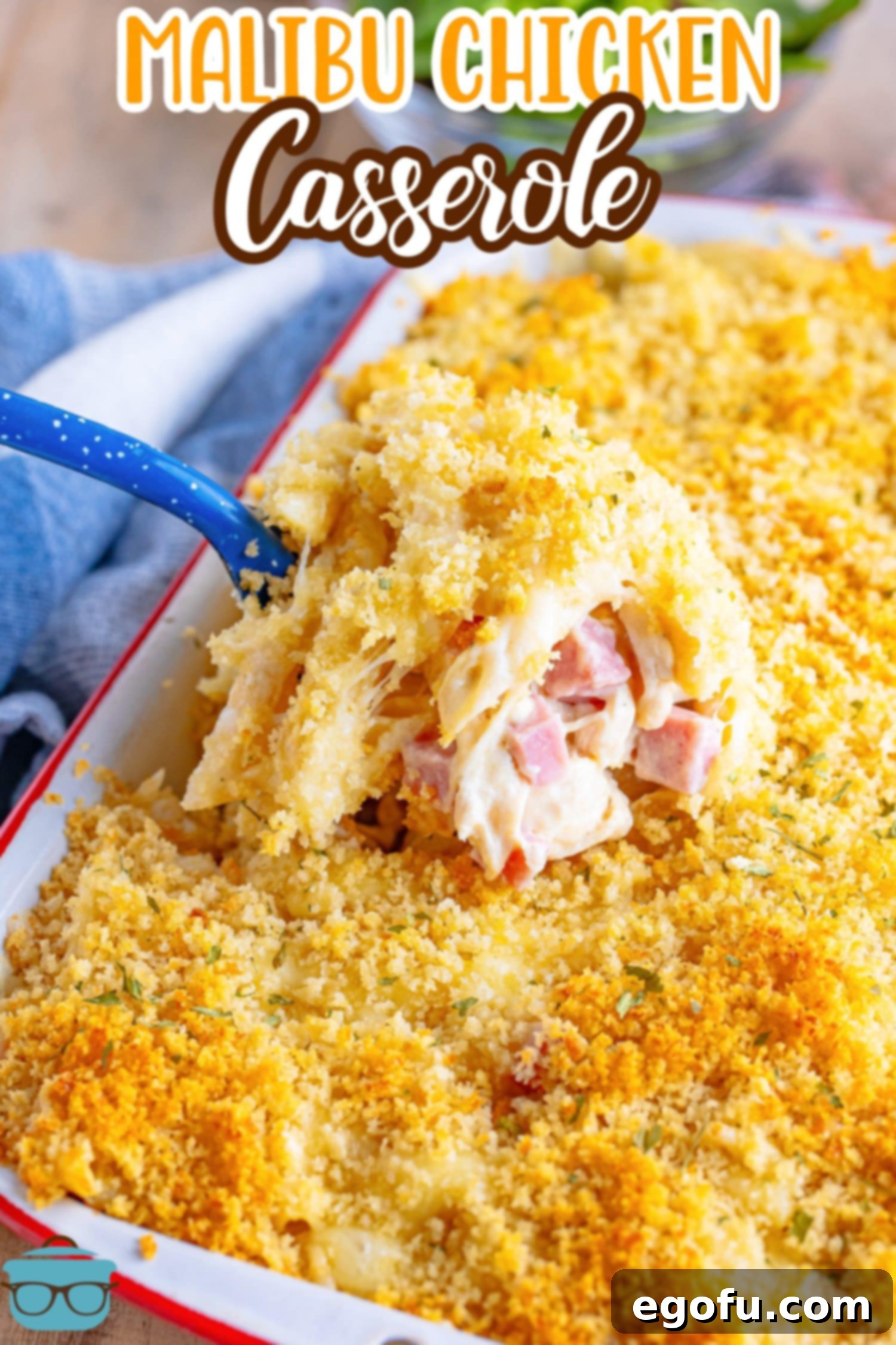 Looking down on a casserole dish with a serving spoon getting a scoop of Malibu Chicken Casserole, showing the gooey cheese and savory chicken and ham.