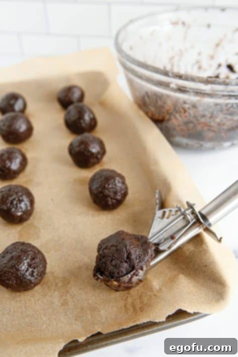 A cookie scoop putting Oreo Balls on a parchment lined baking sheet.