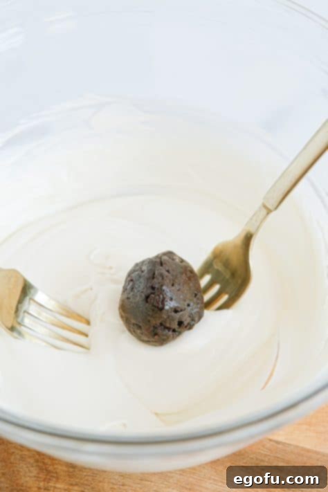Two forks holding a truffle above a bowl of melted white chocolate.