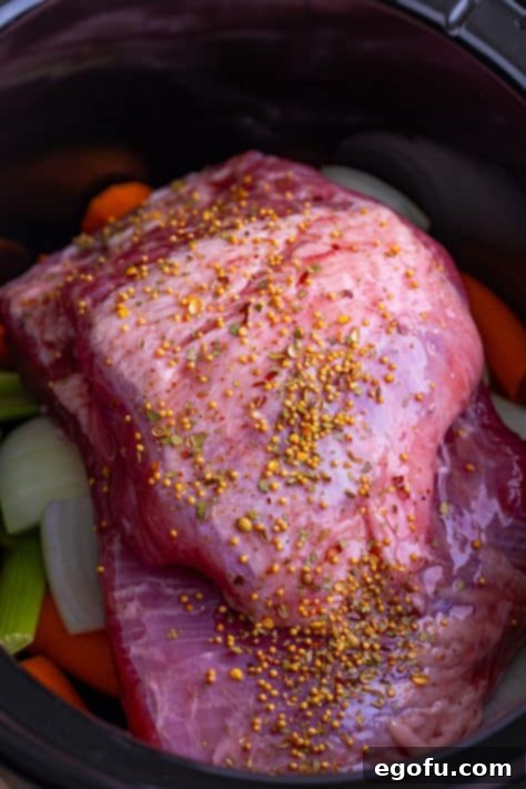 Set-It-and-Forget-It Corned Beef 12 Seasoned beef brisket in a slow cooker on top of vegetables, ready for liquid.