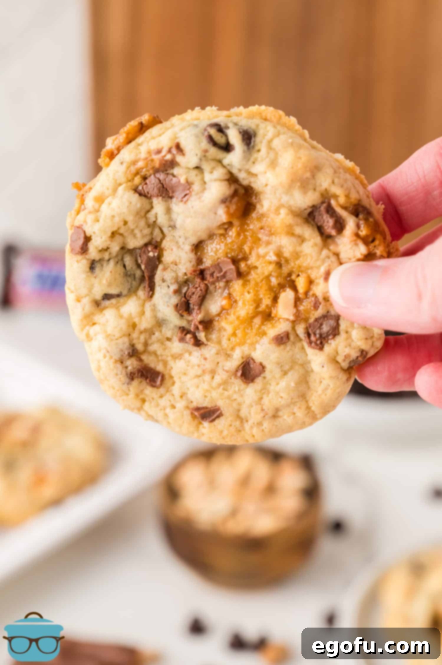 A hand holding a freshly baked Snickers Cookie, highlighting its inviting texture.