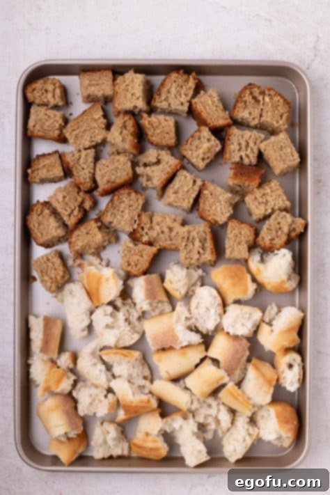 Cubed banana bread and baguette pieces on a baking sheet.