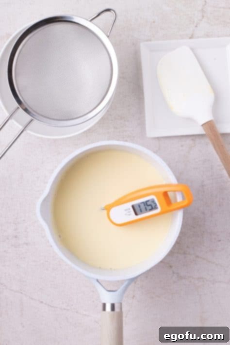 A thermometer in a pan of vanilla sauce, showing it reaching the correct temperature.