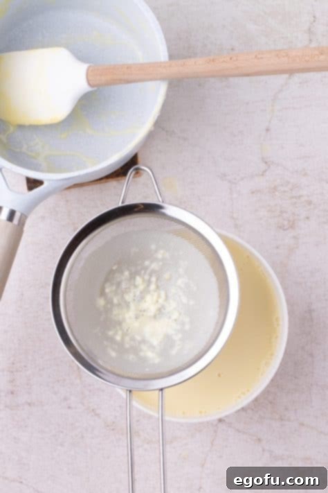 A sieve placed over a bowl, with the vanilla sauce being strained through it for a smooth consistency.