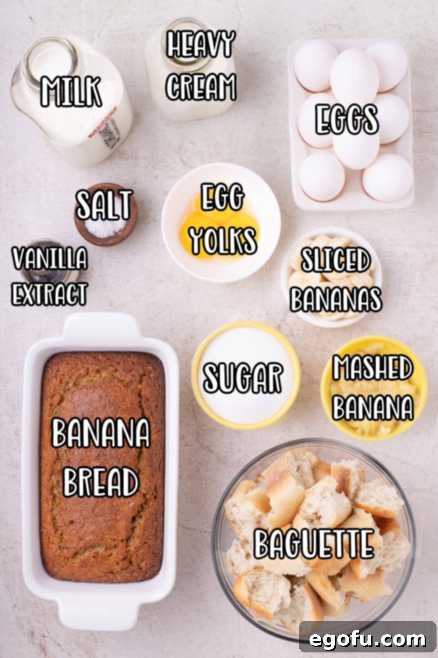 Various ingredients for Banana Bread Pudding laid out: Banana bread, large baguette, heavy cream, whole milk, eggs, egg yolks, salt, vanilla extract, sliced bananas, mashed bananas, and sugar.