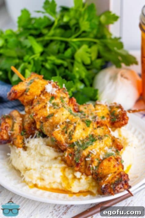 A garlic parmesan chicken skewer on a plate with potatoes.