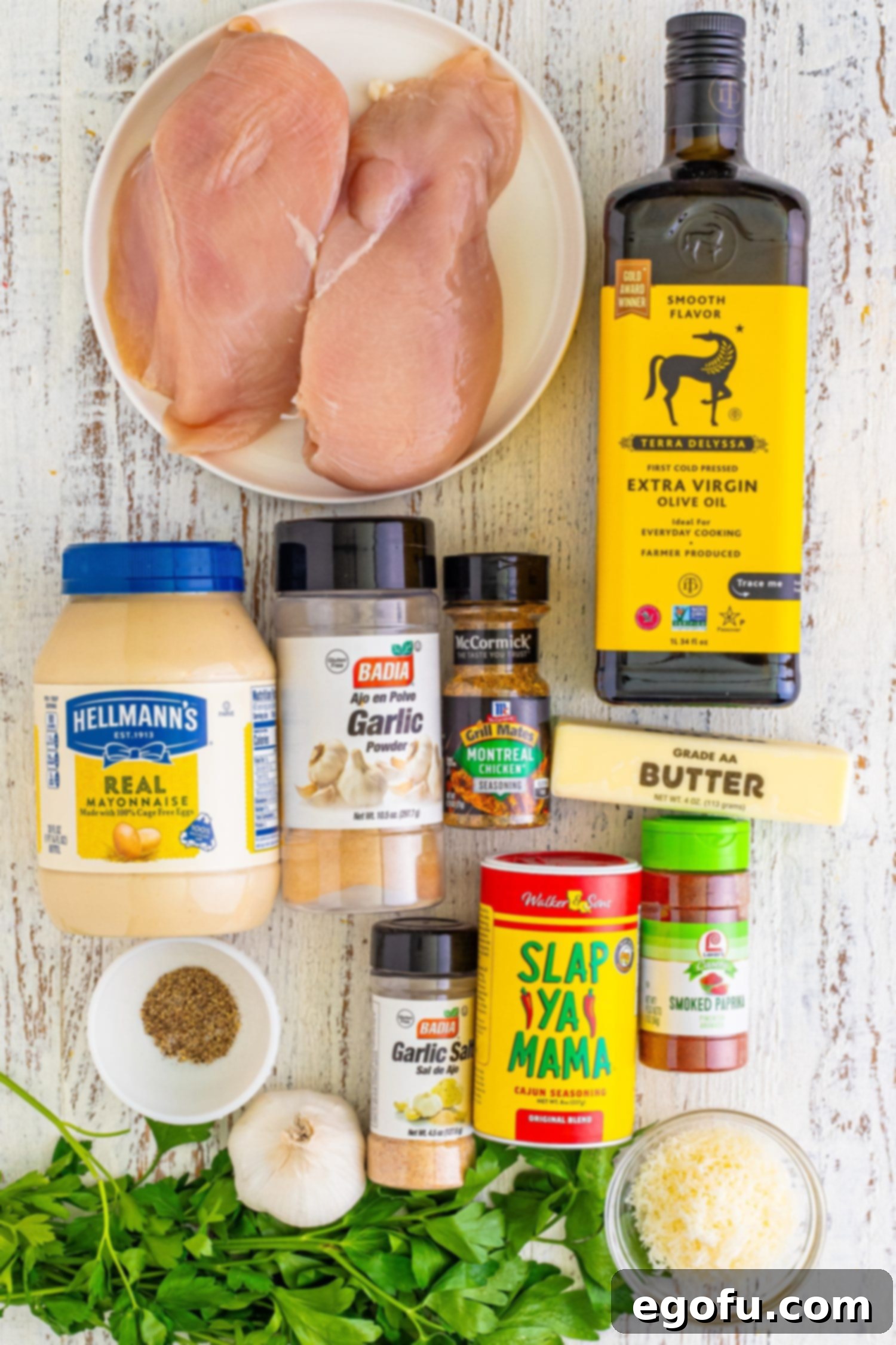 A flat lay photograph showcasing all the fresh and dry ingredients needed for Air Fryer Garlic Parmesan Chicken Skewers: chicken breast, various seasonings, mayonnaise, parmesan cheese, olive oil, butter, and fresh parsley.