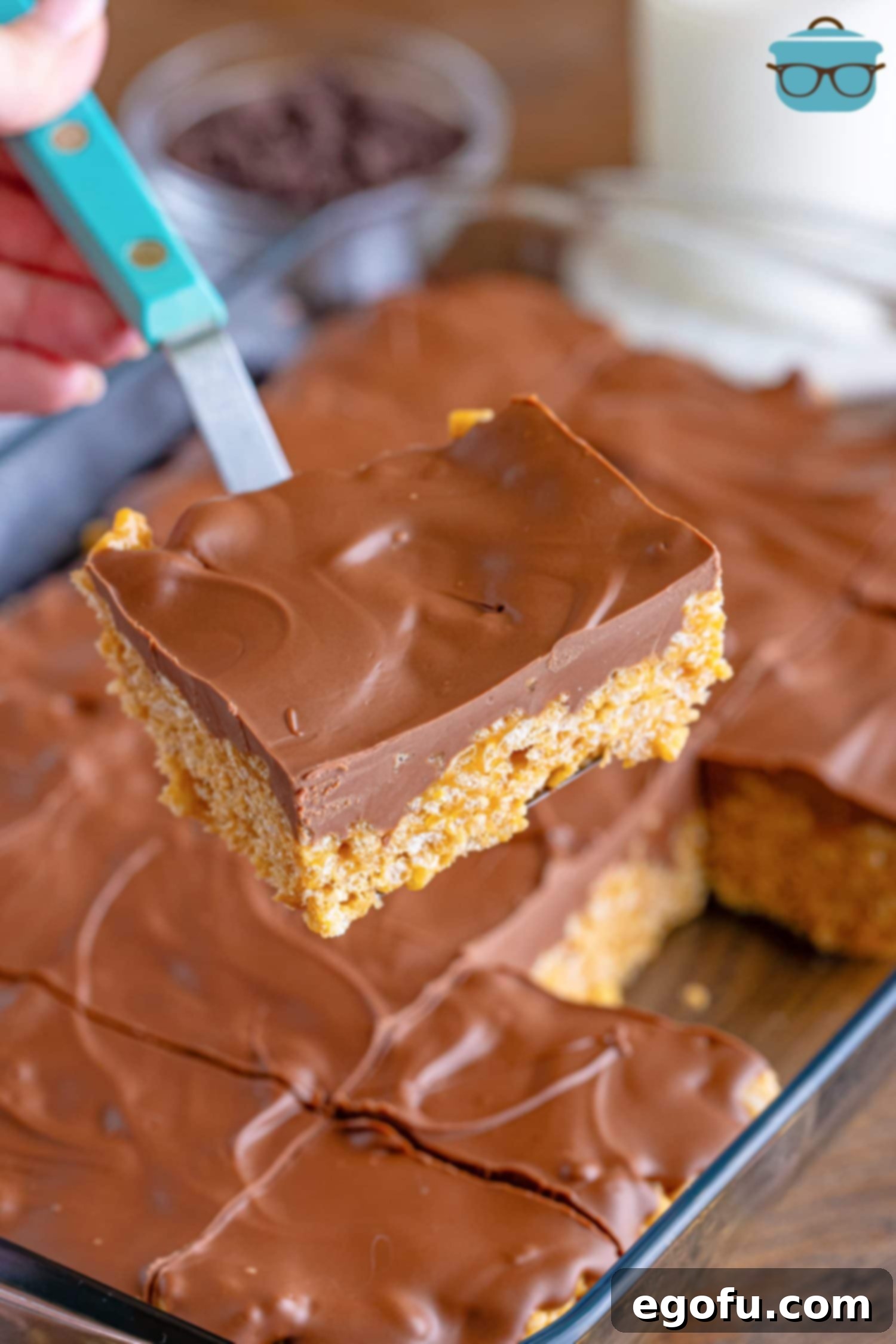 Crispy Peanut Butter Dream Bars 2 A serving utensil holding a Scotcheroo above the pan of the rest of them.