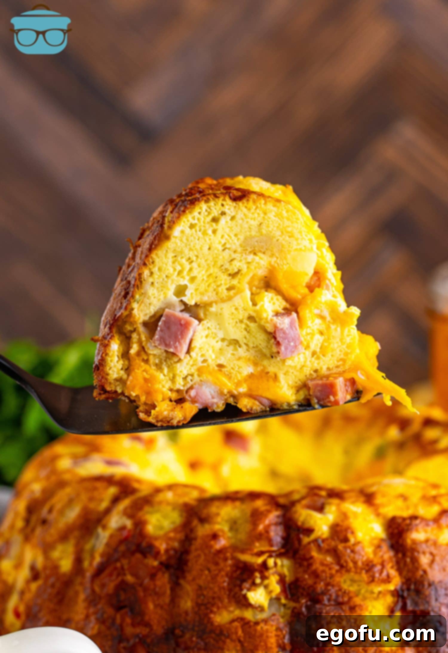 A perfectly sliced piece of golden Breakfast Bundt Cake, showcasing layers of egg, ham, and bread, being lifted from the main cake.