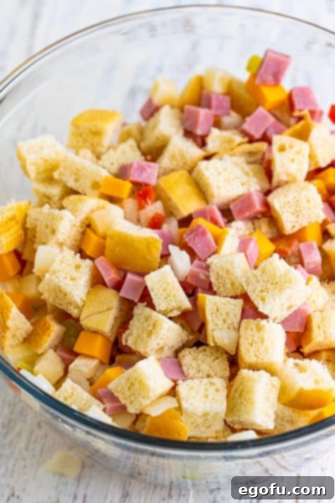 A bowl with bread cubes, cheese, ham, and O'brien Potatoes.