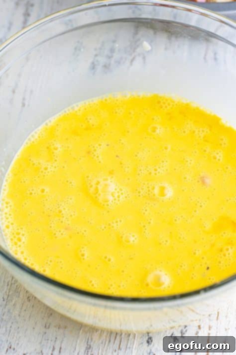 A bowl with eggs, milk, cream, garlic powder, onion powder, salt, and pepper.