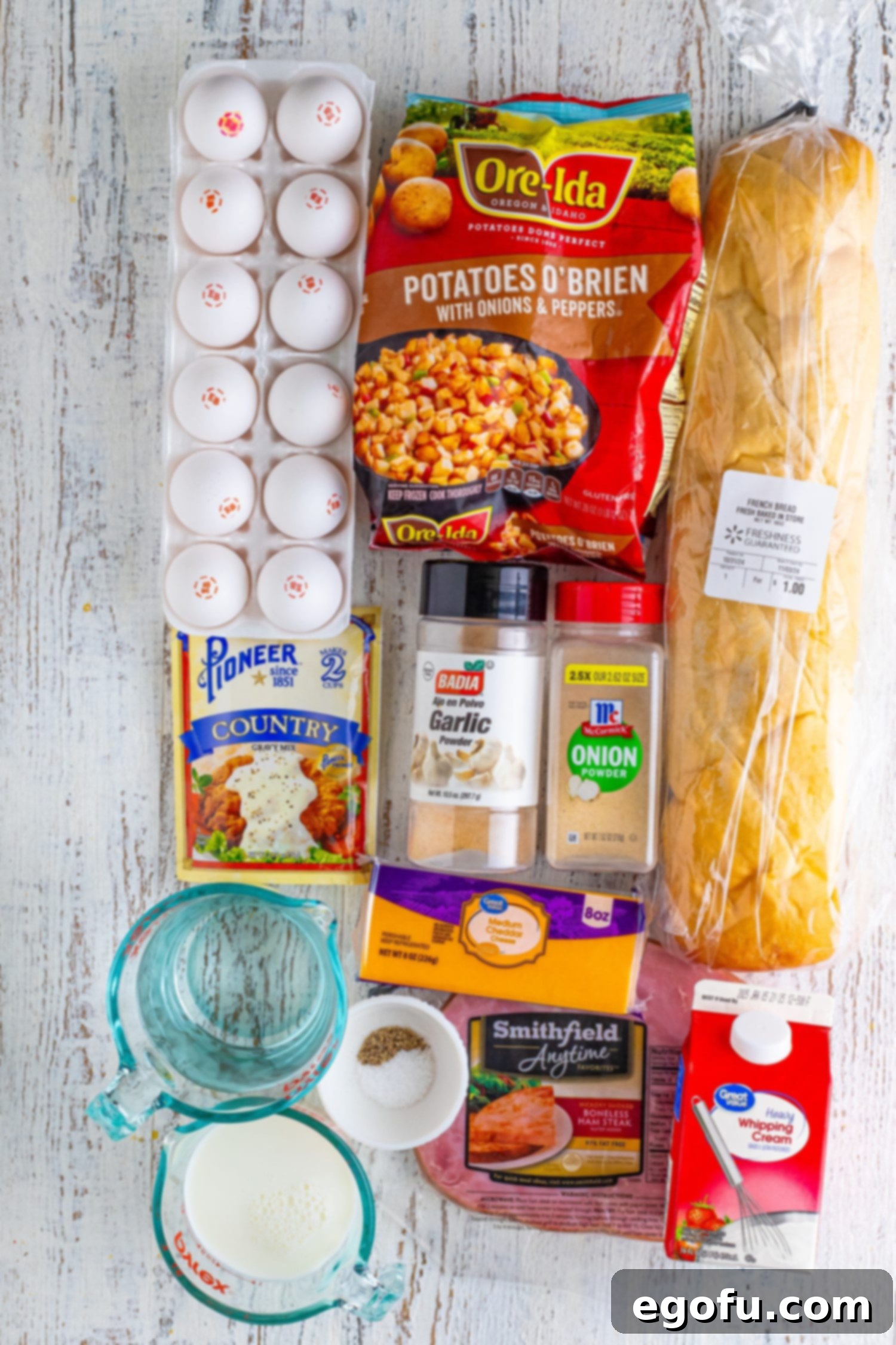 A visual collage of fresh ingredients: eggs, French bread cubes, frozen potatoes O'Brien, diced ham, milk, heavy cream, various spices, water, and an optional gravy packet, ready for the breakfast bundt cake.