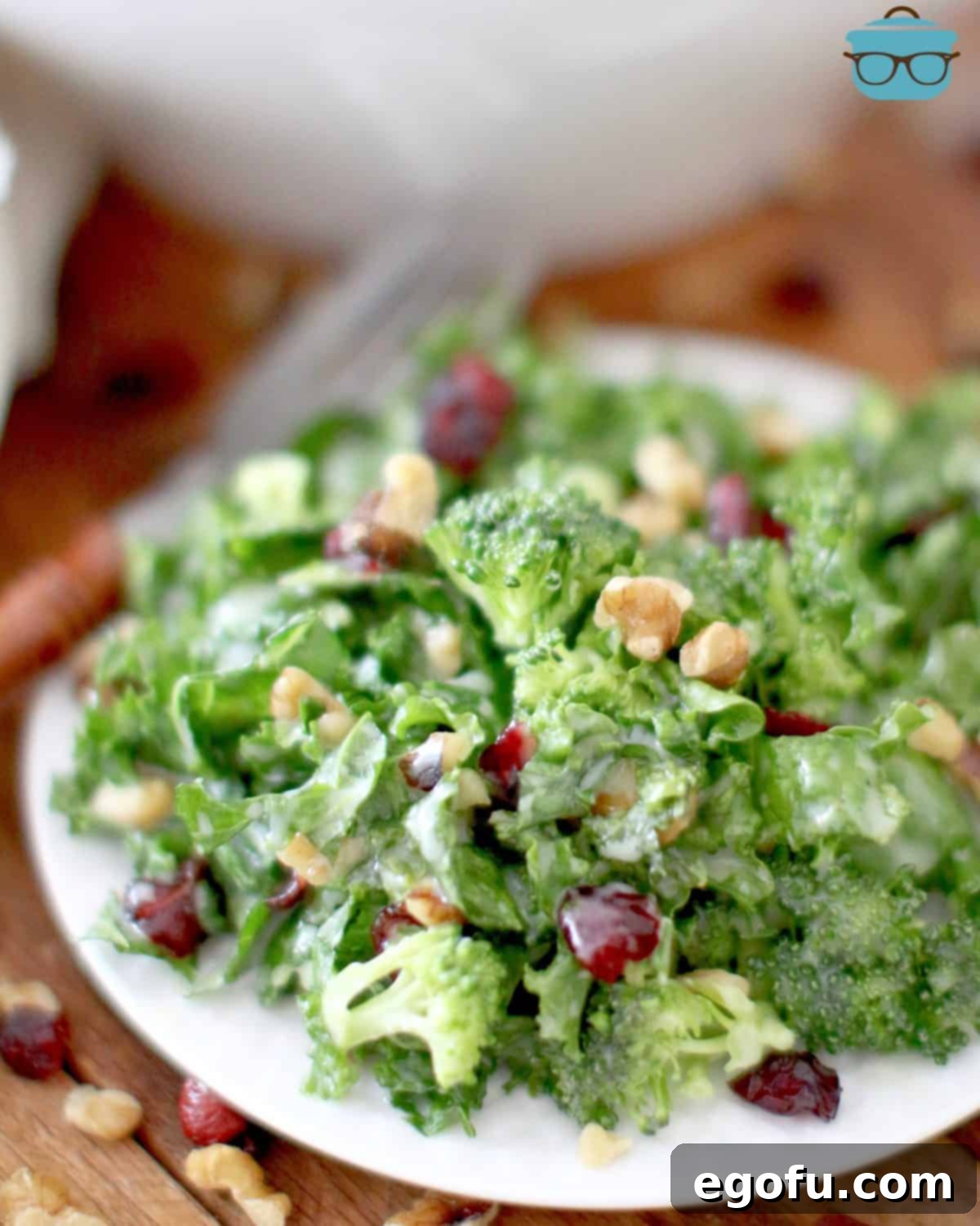 A close-up, overhead view of a single serving of kale salad on a small round white plate, with a fork subtly visible in the background, inviting a taste.