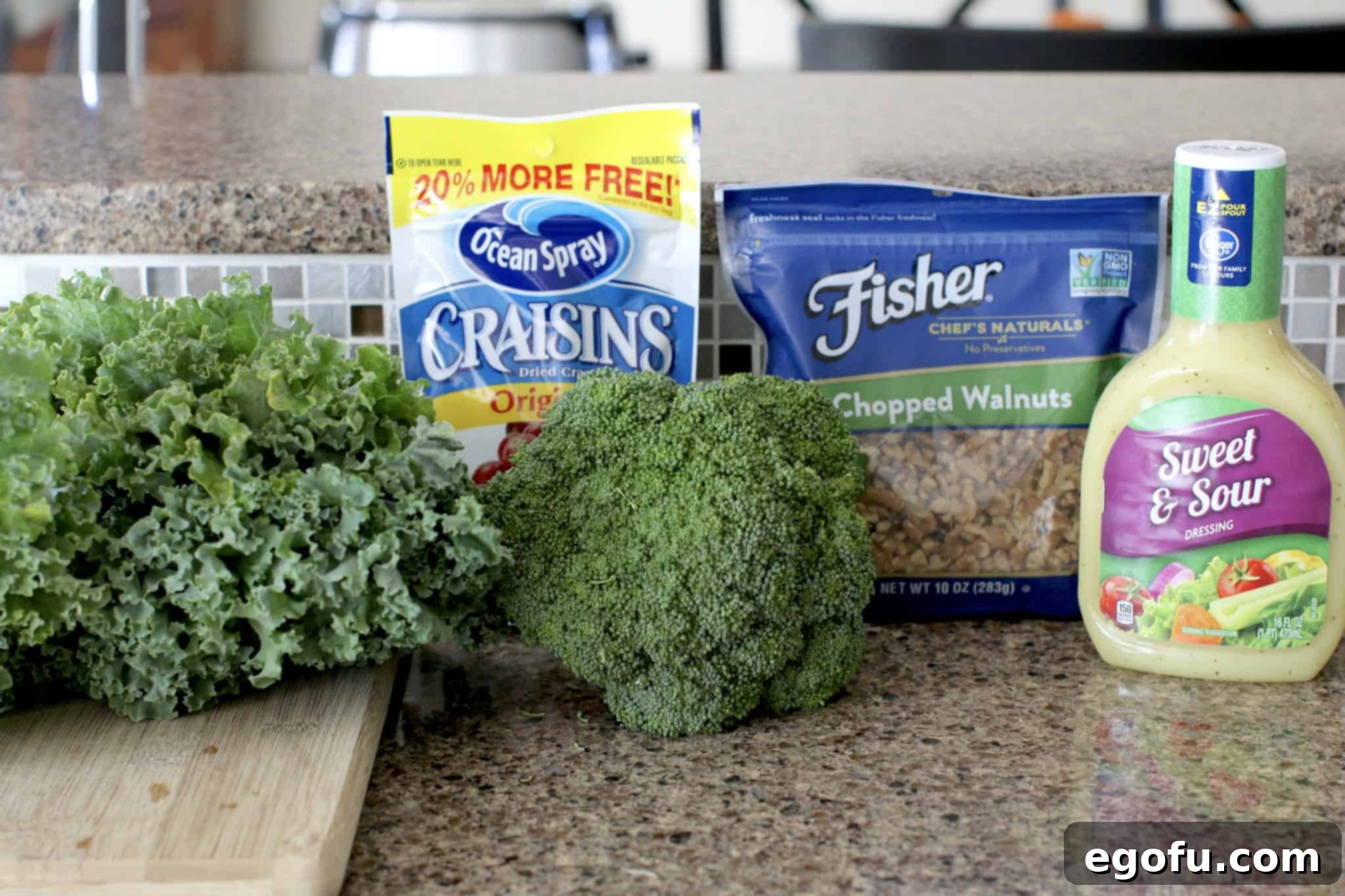 A flat lay photo showcasing the key ingredients for the Copycat Superfood Salad: a bottle of sweet and sour dressing, a pile of chopped walnuts, fresh broccoli florets, and vibrant kale leaves, alongside a scattering of Craisins (dried cranberries).