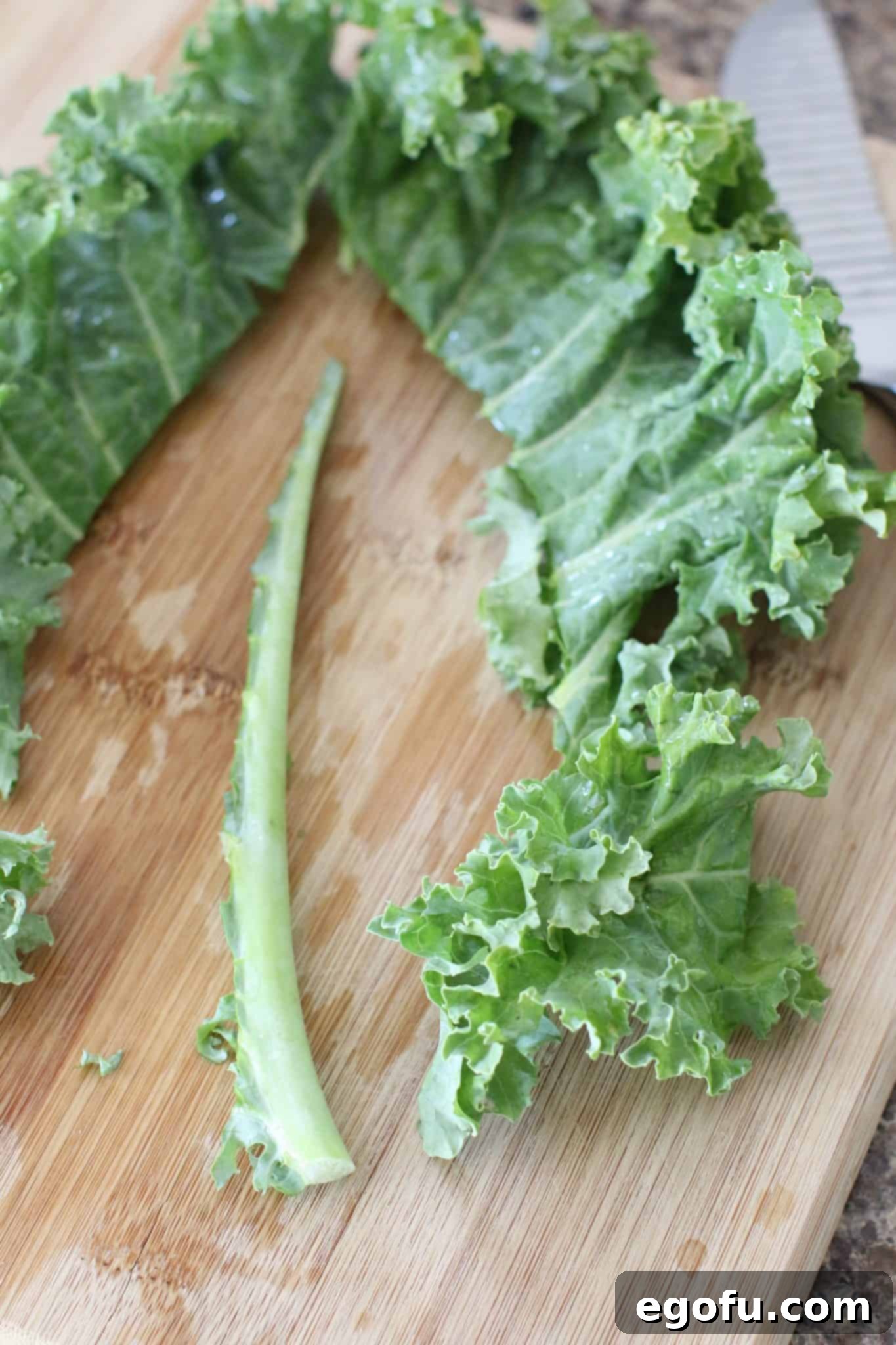 Chopped kale leaves on a wooden cutting board, with the tough central stem neatly cut out and discarded.