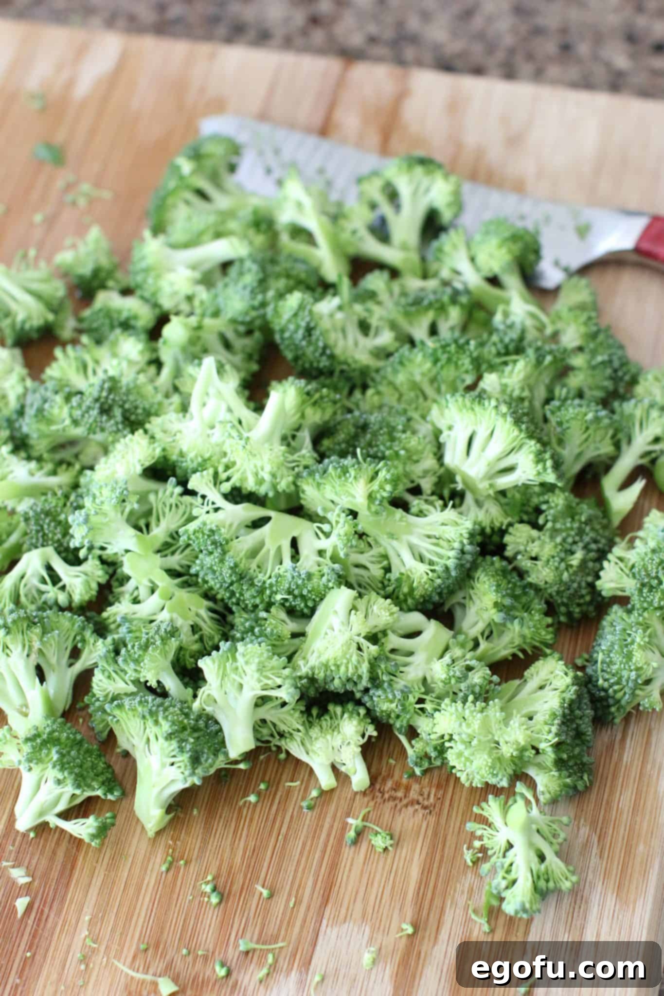 Freshly chopped broccoli florets scattered on a wooden cutting board, prepped for adding to the salad.